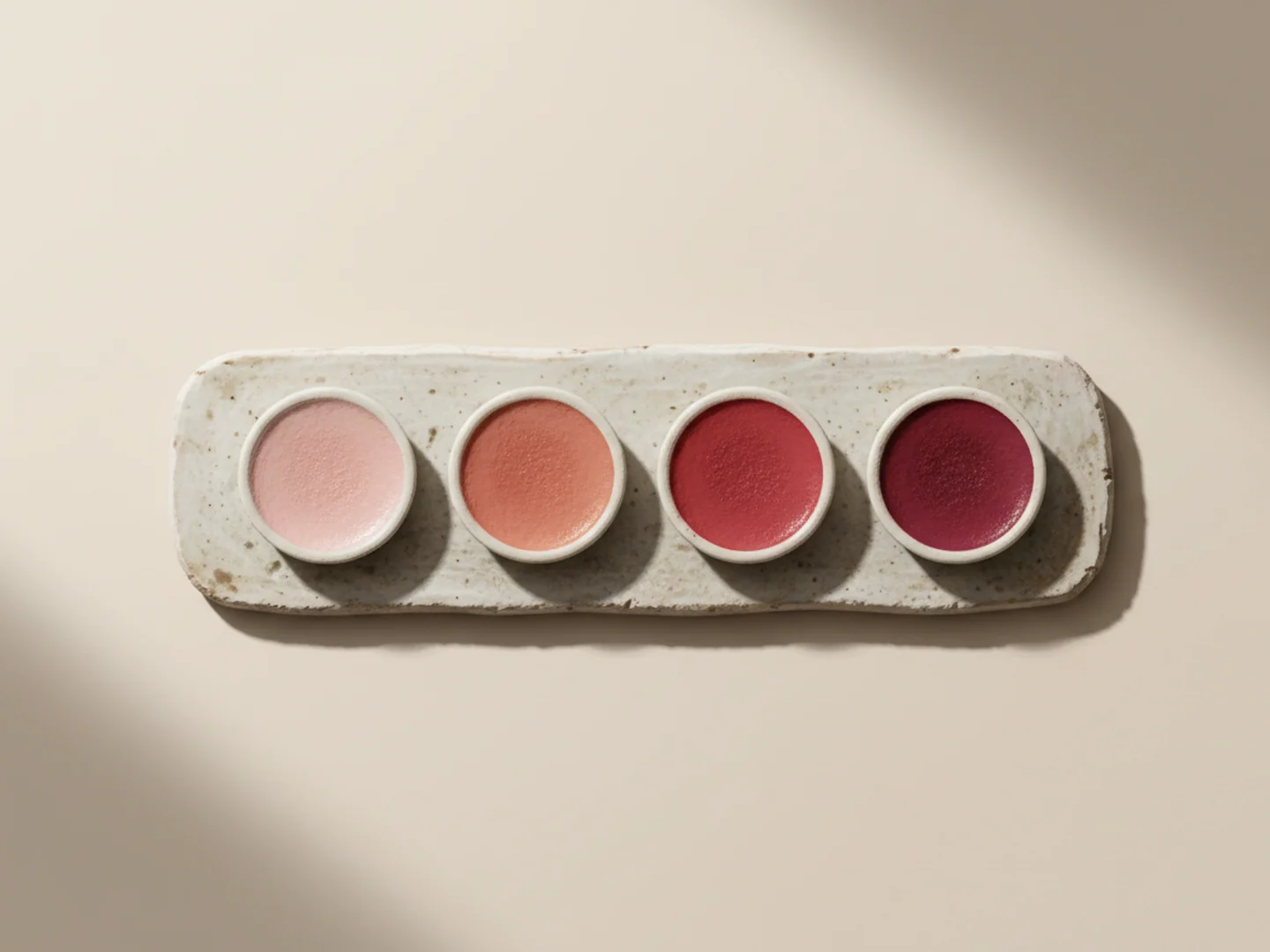 Illustration of four watercolor pans from blush to deep rose lined up on ceramic, the four rosacea phenotypes